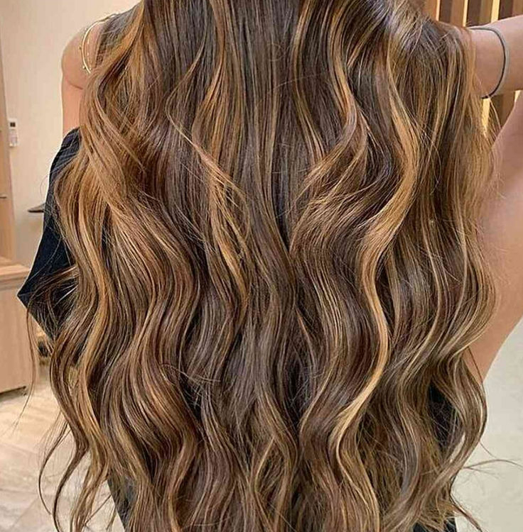 De longs cheveux bruns ondulés aux reflets caramel coulent dans le dos d'une personne, révélant le magnifique résultat de l'utilisation de la Crème Colorante avec Ammoniaque 100 ml, une coloration professionnelle de qualité supérieure et abordable. Dahlia Color Professionnel