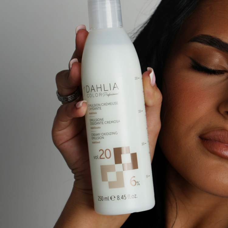 Une femme tient un flacon de révélateur capillaire Dahlia Color Proz Vol. 20 près de son visage, les yeux fermés. Dahlia Color Professionnel