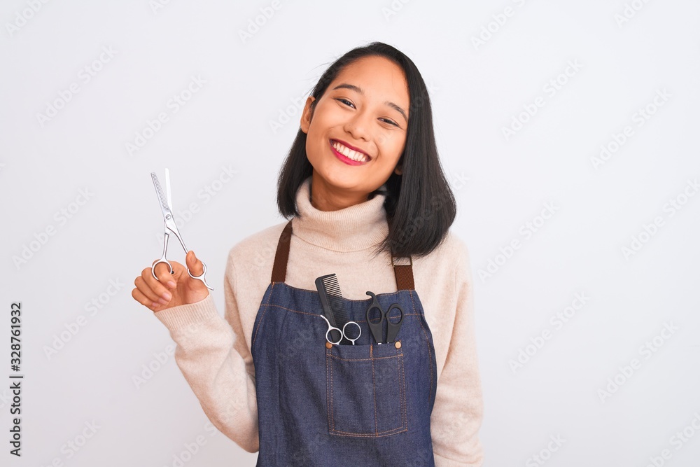 Femme souriante en tablier tenant des ciseaux, avec des peignes et des outils dans sa poche, debout sur un fond blanc. Dahlia Color Professionnel