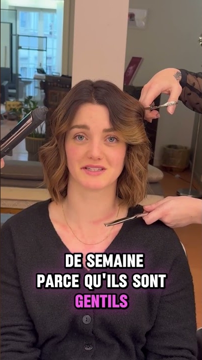 Une femme aux cheveux ondulés est assise sur une chaise de salon pendant que ses cheveux sont coiffés ; texte français superposé. Dahlia Color Professionnel